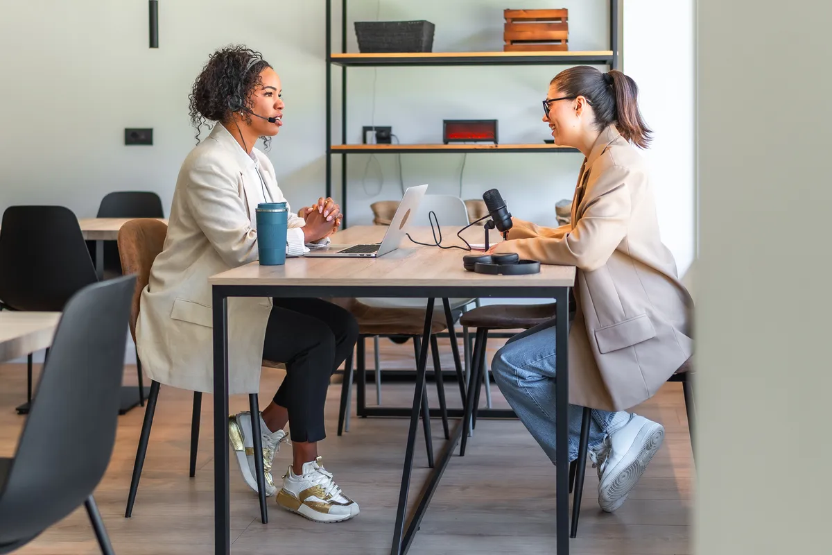 Two colleagues talking across a table, one wearing a headset